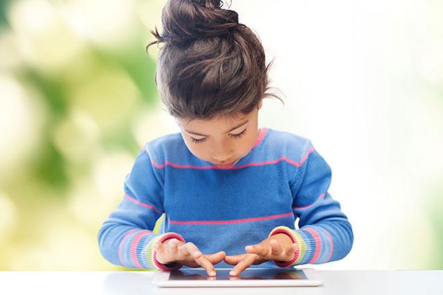一个穿着蓝色毛衣的小女孩在桌子上使用平板电脑