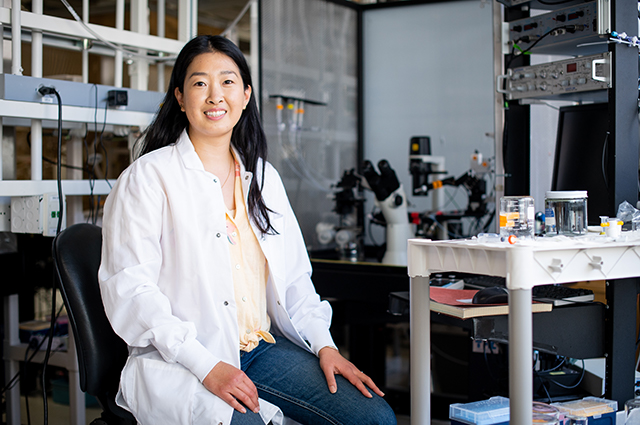 实验室外套的一个女人坐在实验室里。Noell Cho，生物医学科学研究生院博士学生，导师其他第一代大学生，太平洋岛民和科学妇女。